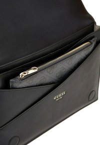 Borsa a tracolla in pelle nera con un compartimento interno testurizzato. Presenta una cerniera dorata e un logo. Design pulito e minimale con una patta ripiegata.
