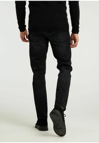 Pantalones vaqueros de mezclilla negra con corte slim, diseño de cinco bolsillos y costuras sutiles. Combinados con zapatos de ante negros que muestran una suela texturizada.