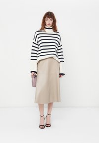 Maglione a collo alto a righe in crema e blu navy, abbinato a una gonna midi in pelle beige. Tacchi neri con cinturini e una piccola borsa lavanda.