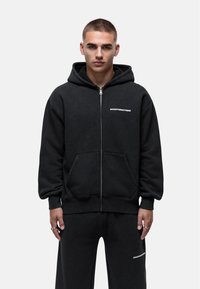 Felpa nera con zip realizzata in cotone, dotata di tasca frontale e caratterizzata da un logo bianco "GOODFORNOTHING" sul petto. Texture morbida e vestibilità rilassata.