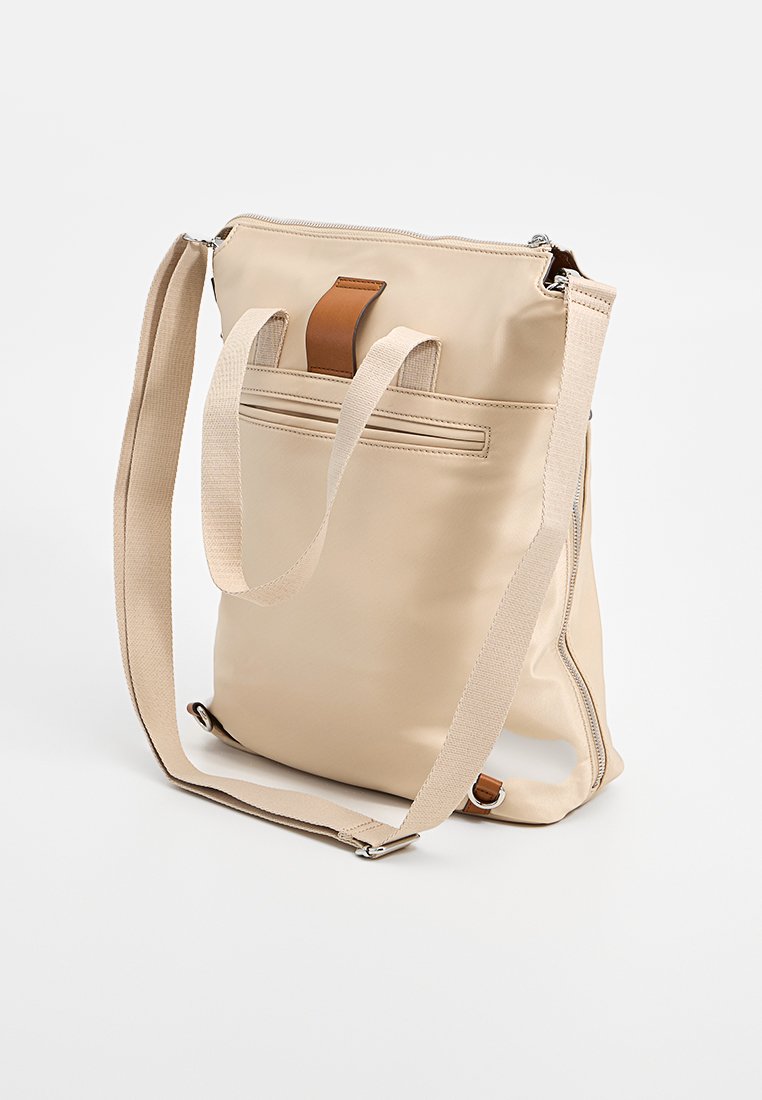Beige Einkaufstasche aus glattem Stoff mit einer weichen Textur, ausgestattet mit einem braunen Lederakzent, verstellbarem Trageriemen und Reißverschluss.