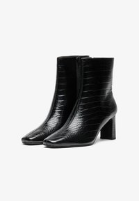 Botine negre până la gleznă cu un model texturat de crocodil, vârf pătrat și toc pătrat. Se închid cu un fermoar lateral. Finisaj neted.