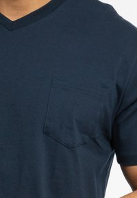 Marineblaue Baumwoll-T-Shirt mit V-Ausschnitt und kleiner Brusttasche, das eine weiche Textur und saubere Nähte aufweist.