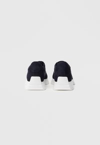 Ζευγάρι ναυτικό μπλε αθλητικά παπούτσια με χοντρές λευκές πλατφόρμες, εμφανιζόμενα από πίσω σε απλό ανοιχτό γκρι φόντο.