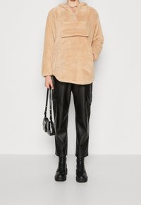Pullover in pile beige con collo a mezza zip e tasca frontale, abbinato a pantaloni cargo in pelle nera e stivali neri chunky.