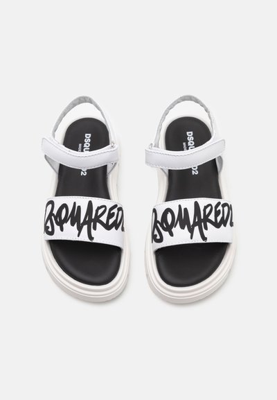 Vita sandaler med svart text "DSQUARED2" över den breda överskon. Har en dämpad svart innersula och vit gummisula.