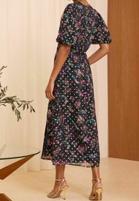 Blommig, svart midi-klänning med puffärmar och åtdragen midja. Tyget har livliga rosa och gröna mönster. Kommer med guldfärgade klacksandaler.