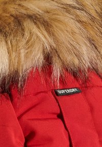 Rode pufferjas met een afneembare faux fur kraag. Zwarte "SUPERDRY" label op de stof, met een quilted ontwerp.