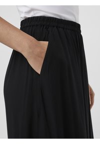 Pantalón negro, ligero, con cinturilla elástica y bolsillos laterales. Textura suave, corte recto y diseño hasta el tobillo.