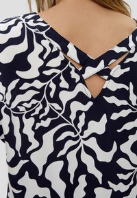 Vêtement à motif floral bleu marine et blanc avec un dos en forme de V présentant des détails en croisillons et un tissu texturé.