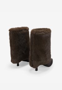 Botas de tobillo de pelo marrón con punta redonda y tacón bajo. Las botas presentan una textura suave y esponjosa y un color marrón intenso.
