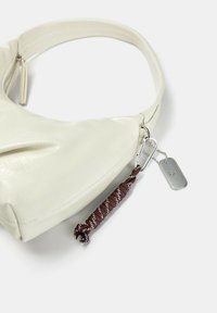 Weißer Kunstlederbeutel mit runder Form, strukturiertem Oberflächenmaterial und einem abnehmbaren Schlüsselanhänger aus braunem und weißem Schnur. Mit silberner Hardware.
