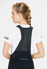 Schwarze athletische Trägershorts mit Netzträgern, ausgestattet mit reflektierenden Logos auf der Rückseite und einem weißen, atmungsaktiven kurzärmeligen Oberteil.