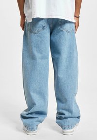 Behagelige, lyseblå denimjeans med en falmet tekstur, store baklommer og mansjetter som hviler på hvite sneakers.