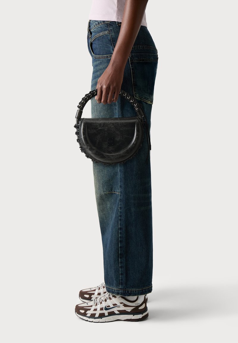 Sac à main en cuir noir avec une forme semi-circulaire et une surface texturée, présentant un design de poignée unique et un subtil détail de logo.