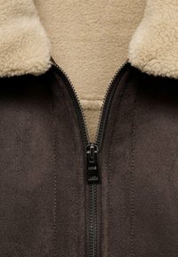 Brunfärgad faux suede-jacka med en krämfärgad shearlingkrage, med en central blixtlås och sydda detaljer längs sömmarna.