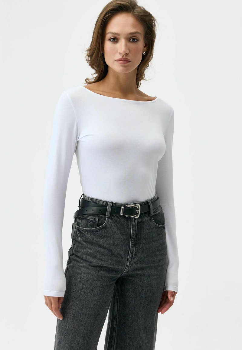 Biała bluzka z długim rękawem i dekoltem w łódkę, zestawiona z czarnymi, wysokim stanem jeansami oraz czarnym paskiem z srebrną klamrą.