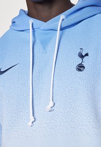 Felpa leggera blu con texture a gradiente, caratterizzata da un logo scuro di un uccello e una palla, e cordini bianchi per una vestibilità regolabile. Logo Nike sul petto.