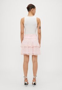 Haut sans manches blanc avec une jupe superposée à fleurs roses, dotée d'une ceinture smockée. Des talons avec des brides blanches complètent la tenue.