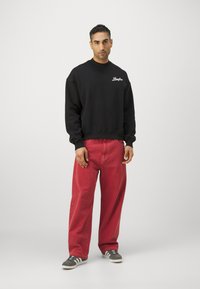 Sudadera negra con texto blanco, pantalones rojos holgados y zapatillas grises con detalles blancos. Tejido suave con un corte relajado y cuello redondo.