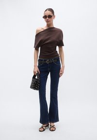 Καφέ τοπ που αφήνει τους ώμους ακάλυπτους, καμπανέ σκούρο μπλε τζιν, μαύρη ζώνη με καρφιά, μαύρη τσάντα χειρός και μαύρα σαγιονάρες με λεπτά λουράκια.