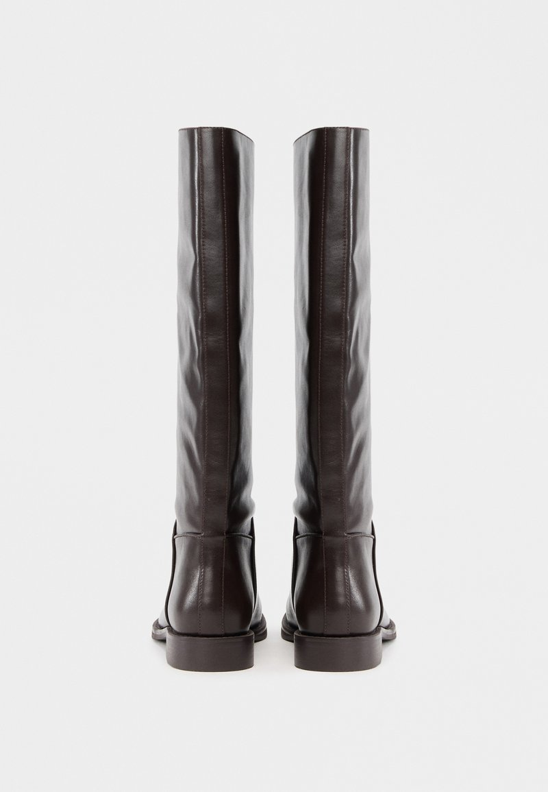 Braune kniehohe Stiefel aus Leder mit glatter Textur, vertikalen Nähten und einem niedrigen Blockabsatz. Sie haben ein minimalistisches Design.