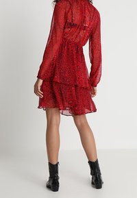 Robe rouge en voile transparent avec un motif léopard, jupe à volants, manches longues, taille cintrée, portée avec des bottines noires.