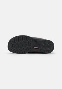 Semelle de chaussure noire présentant un motif de grip texturé et un logo KEEN bien visible, sur fond blanc uni.