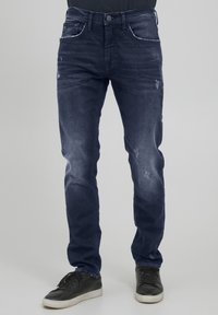 Mörkblå denimjeans med smal passform, med bleka lappar och lätt slitage. Femfickdesign, med vita sömmar som detalj.