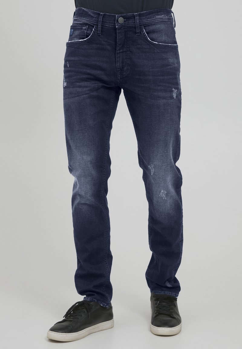 Mörkblå denimjeans med smal passform, med bleka lappar och lätt slitage. Femfickdesign, med vita sömmar som detalj.