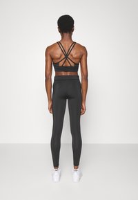 Svart atletisk outfit med en sportbh med korsade band på ryggen och högmidjade leggings, i kombination med vita sneakers.