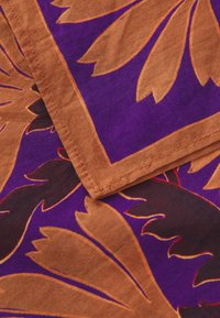 Cotton fabric featuring a bold purple background with large brown leaf patterns and contrasting red outlines; neatly stitched edges.
