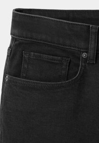 Gros plan sur un jean en denim noir avec poche avant visible, poche pour pièces, passants de ceinture et rivets métalliques sur la ceinture et la poche.