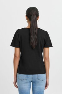 T-shirt nera in cotone con maniche corte, scollatura a giro e taglio dritto, abbinata a jeans in denim blu chiaro.