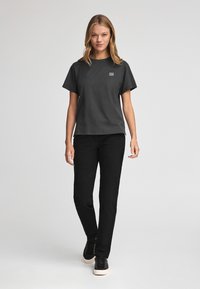 Svart bomulls t-shirt med korta ärmar, rund halsringning och ett patch-logotyp på vänster bröst, i kombination med svarta raka byxor och svarta sneakers.