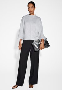 Maglione grigio a maniche lunghe con colletto alto, abbinato a pantaloni neri a gamba larga e una pochette metallica argento. Texture liscia e design semplice.