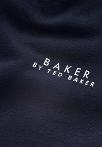Marinblått tyg med en slät yta som har den vita tryckta texten "BAKER by TED BAKER" tydligt visad.