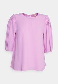Blouse lavande avec encolure ronde et manches trois-quarts bouffantes présentant des détails plissés sur les épaules et une petite fermeture à bouton dans le dos.