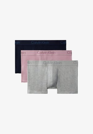 Gespiereerde man staat blootsvoets in zwarte Calvin Klein boxershorts tegen een effen lichtgrijze achtergrond.