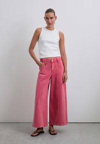Jeanși din denim roz cu picioare largi, prevăzuți cu buzunare frontale și un talie înaltă, asortați cu un top strâns din bumbac alb cu dungi. Textură netedă, croială lejeră.