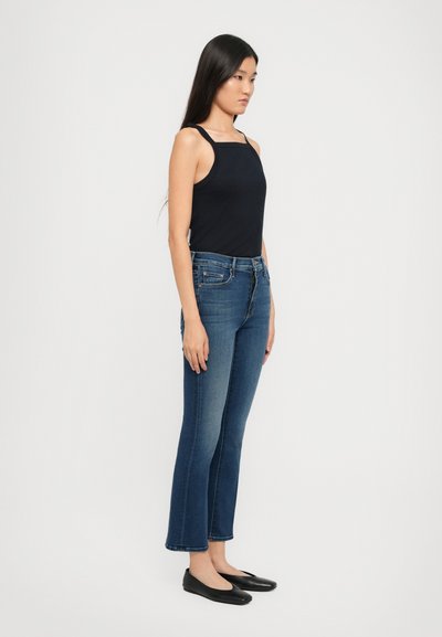 Marineblauwe top met spaghettibandjes gecombineerd met donkerblauwe flared jeans. Soepele stof, aansluitende top, subtiele stiksels en zwarte ballerina's.