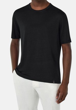 Černé tričko z měkké, lehké látky s kulatým výstřihem a volným střihem, doplněné o bílé lněné kalhoty. Malý logo akcent na lemu.