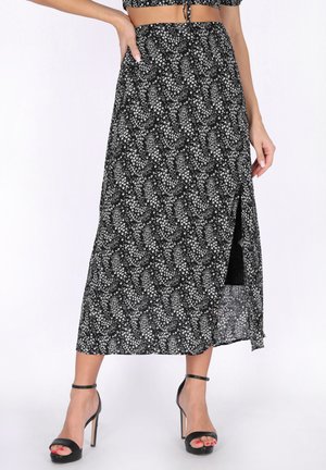 Gonna midi nera con motivo floreale bianco e spacco laterale, indossata con sandali neri con cinturino alla caviglia e tacchi alti e top corto abbinato.