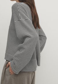 Maglione a righe in bianco e nero con una forma squadrata, spalle cadenti e tessuto texturizzato. Abbinato a pantaloni grigi chiari.