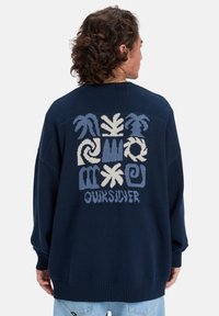 Suéter de malha azul-marinho com um grande design gráfico multicolorido nas costas, com padrões abstratos e o nome da marca "Oursilver" na parte inferior.