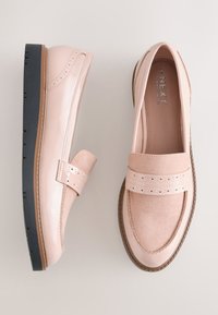 Paire de mocassins rose clair avec textures en daim et cuir verni, détail de bride perforée et semelles en caoutchouc noir sur fond clair.