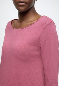 Rozā garroku tops ar apaļu kakla izgriezumu. Izgatavots no mīksta auduma, tam ir gluda virsma un vienkārša, tīra šūšana gar šuvēm.