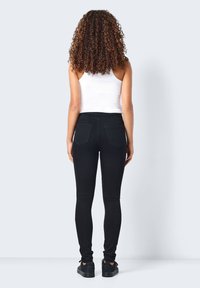 Calças skinny pretas em denim, com dois bolsos traseiros e uma cintura alta, combinadas com uma blusa justa branca.