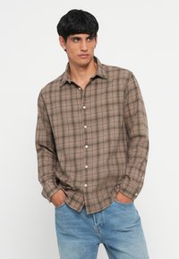 Brun och beige rutmönstrad skjorta med krage, långa ärmar och vita knappar. Bärs med ljusblå denimjeans.