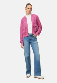 Veste bomber rose duveteuse avec deux poches sur le devant, associée à un jean évasé bleu clair et des baskets blanches. Accents côtelés subtils sur les poignets.